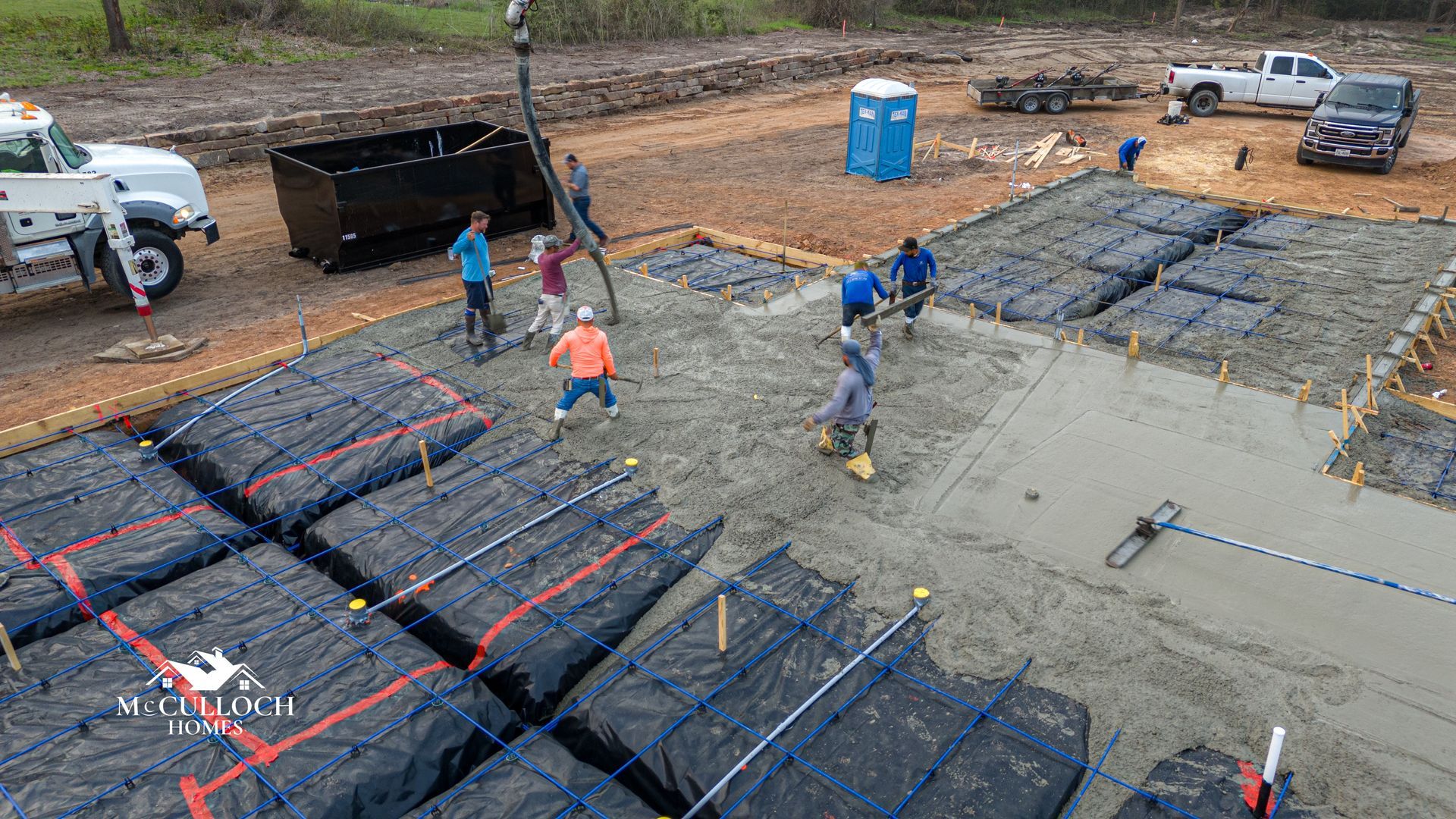 A group of construction workers are working on a concrete base for a house.