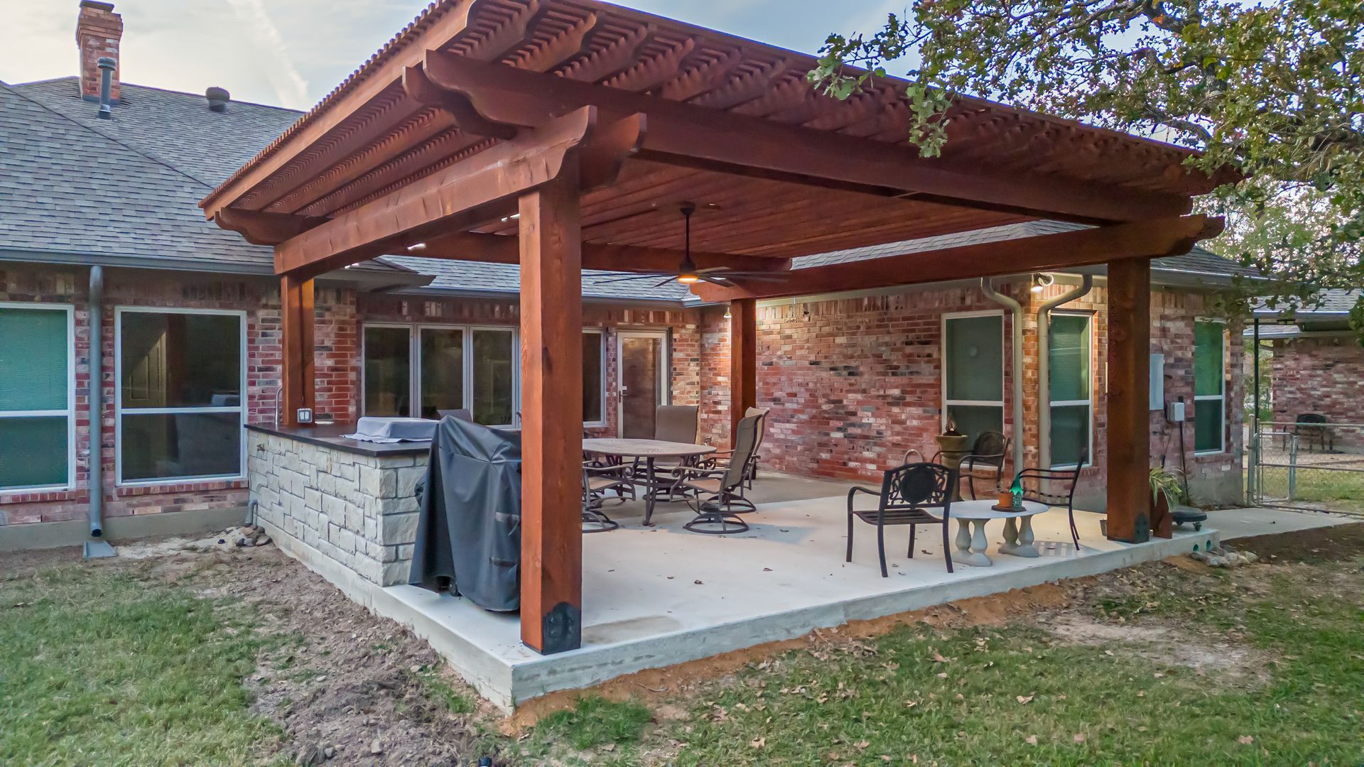 A wooden pergola is sitting on top of a patio in front of a brick house.