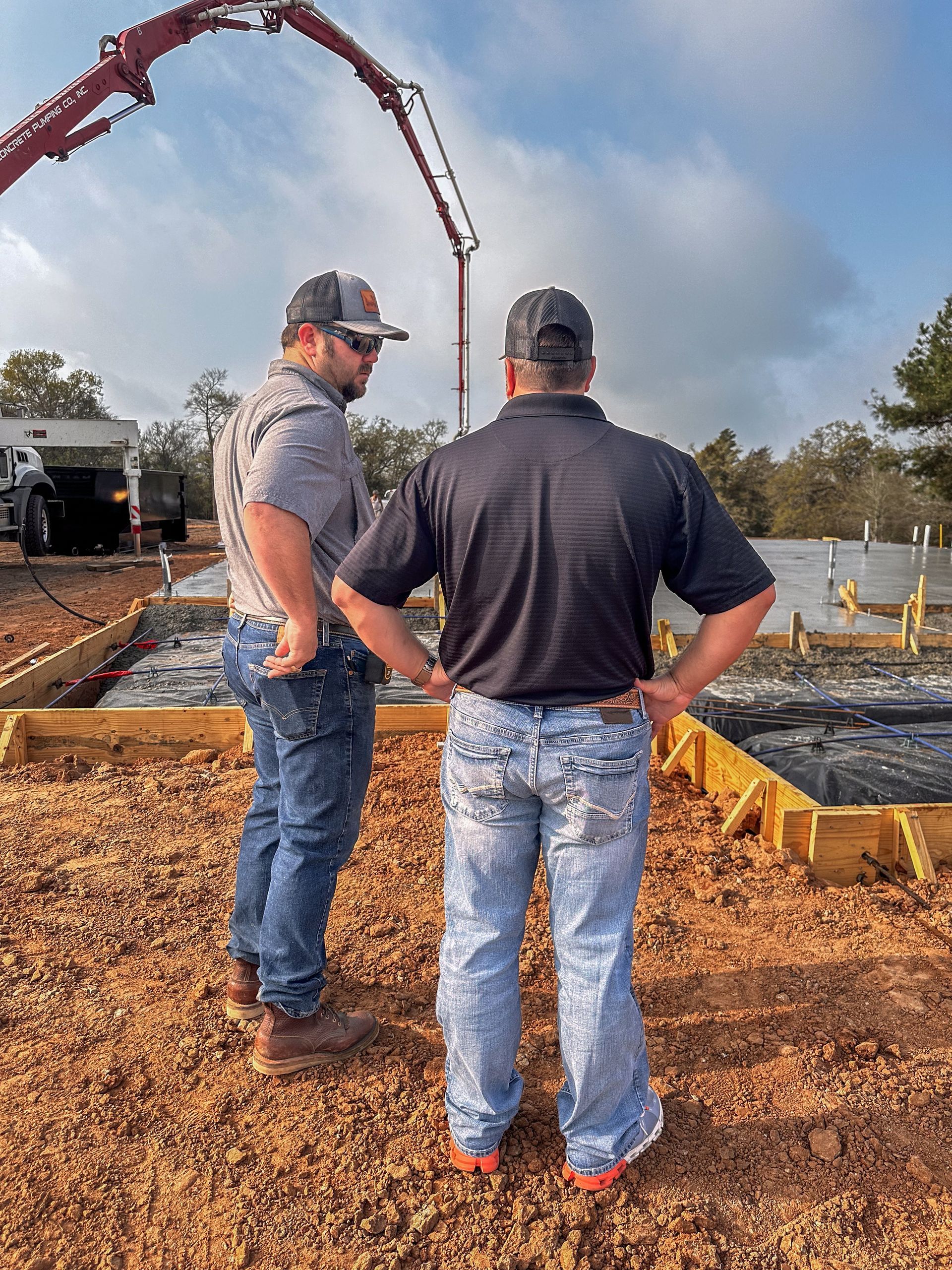 Two men are standing in front of a concrete pump on a construction site.