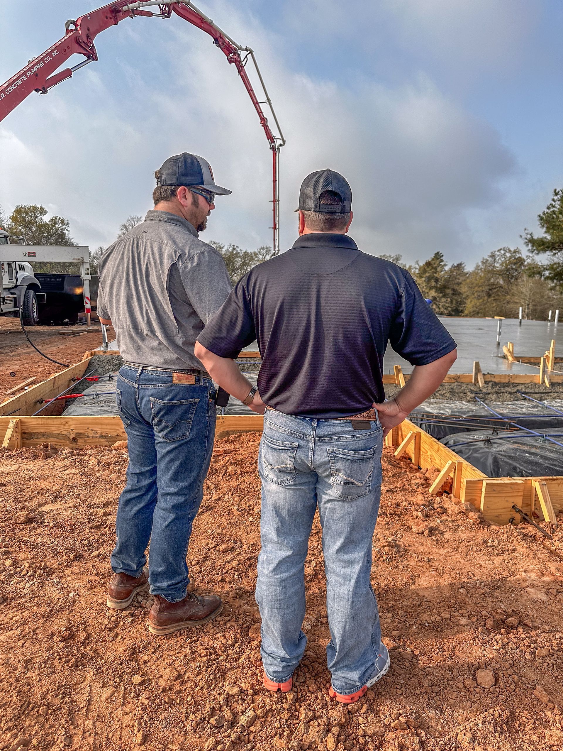 Two men are standing in front of a concrete pump on a construction site.