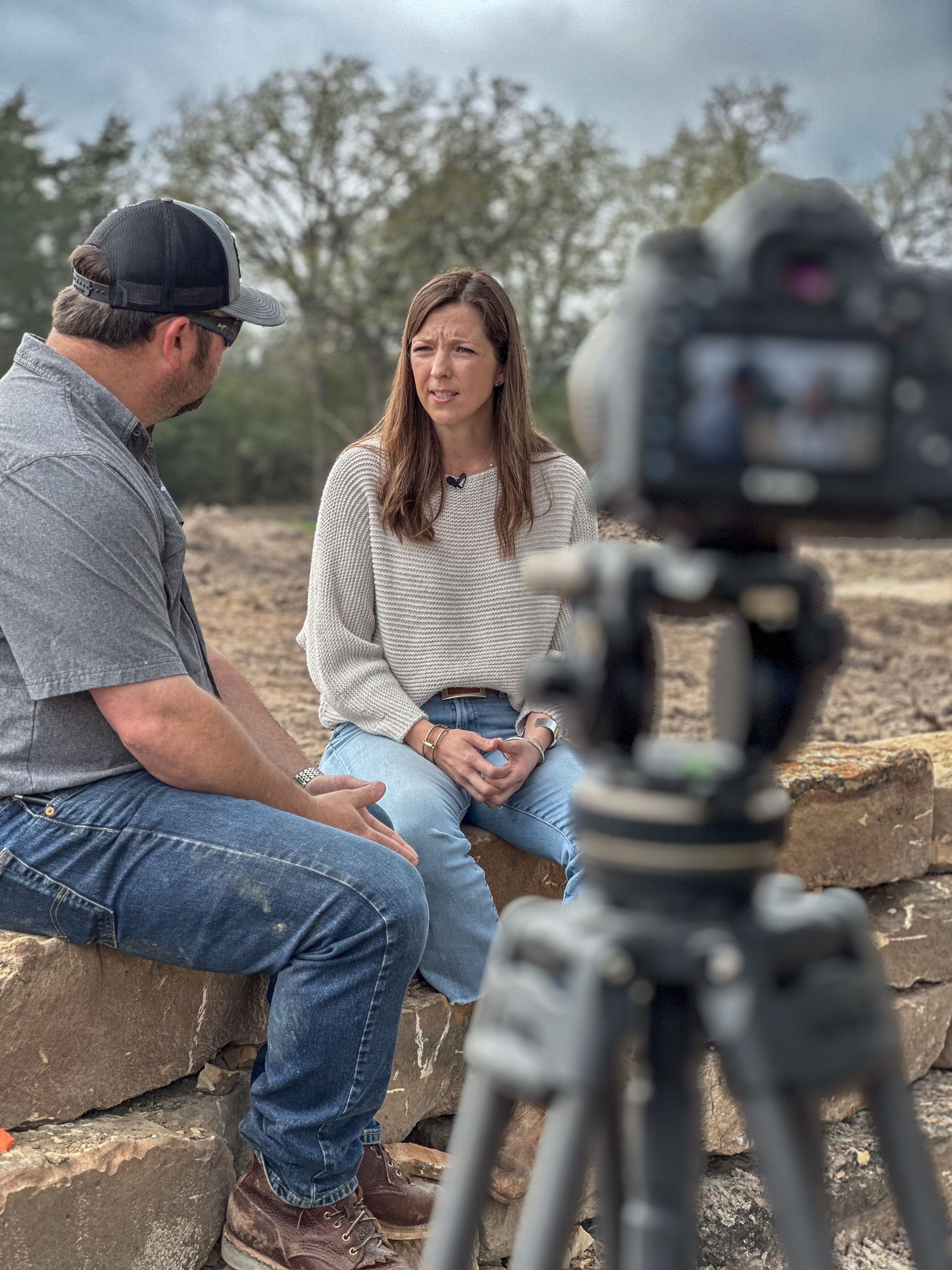 A man and a woman are sitting on a rock talking to a camera.