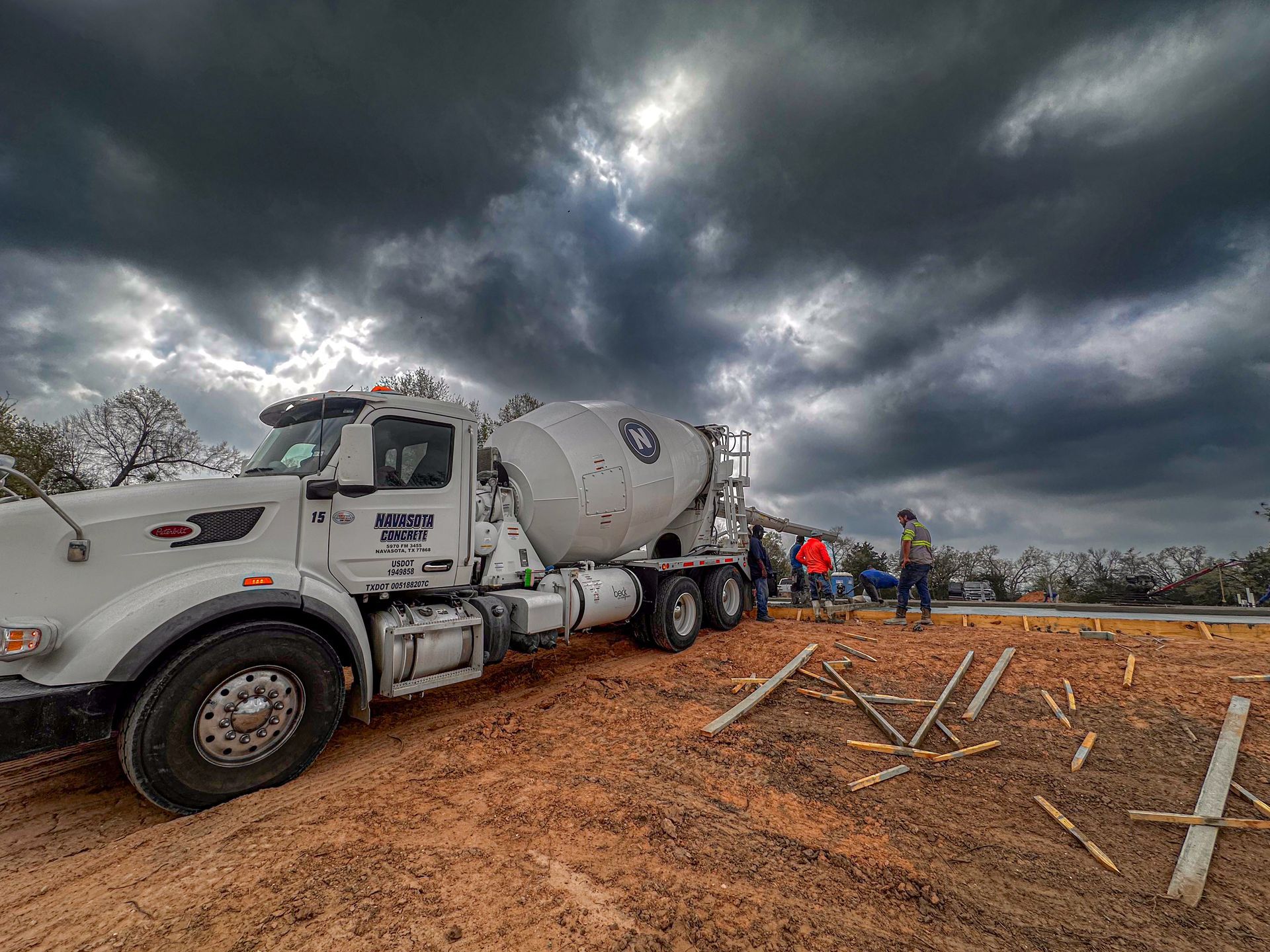 A concrete mixer truck is parked in a dirt field under a cloudy sky.