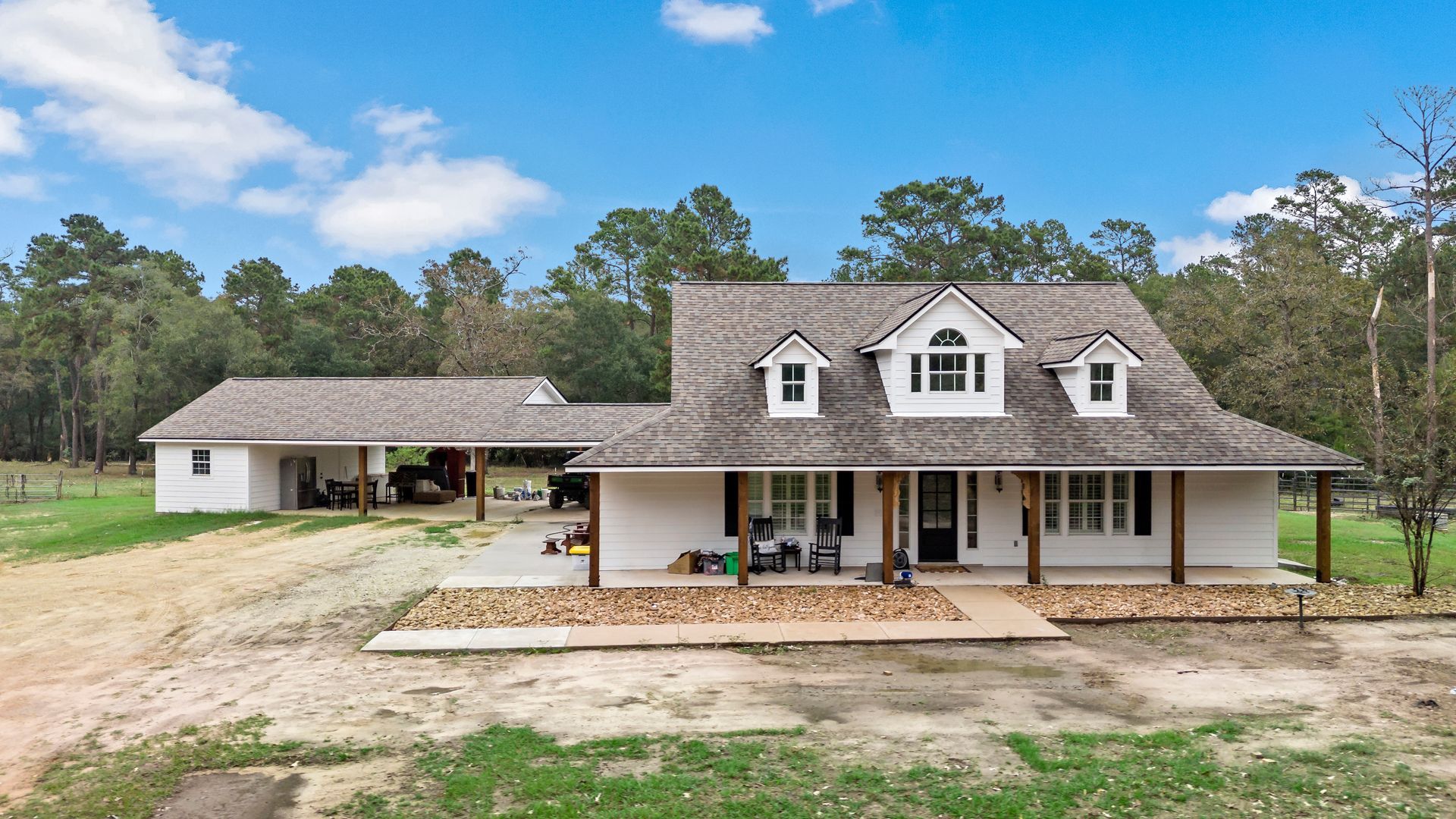 A large white house with a porch in the middle of a field.