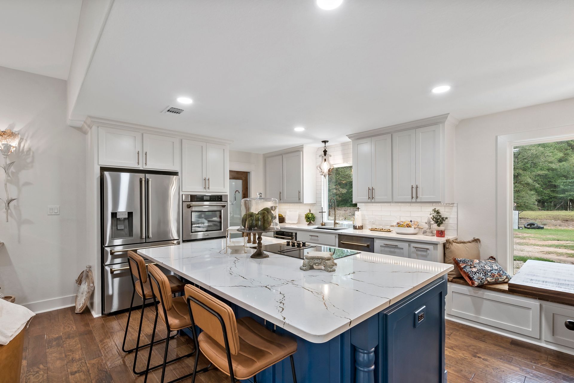 A kitchen with a blue island , white cabinets , stainless steel appliances , and a window.
