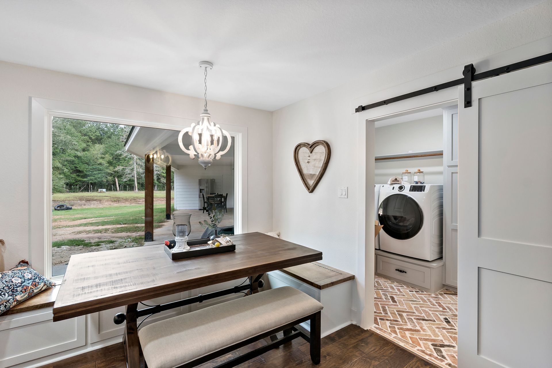 A dining room with a table and bench and a sliding barn door leading to a laundry room.