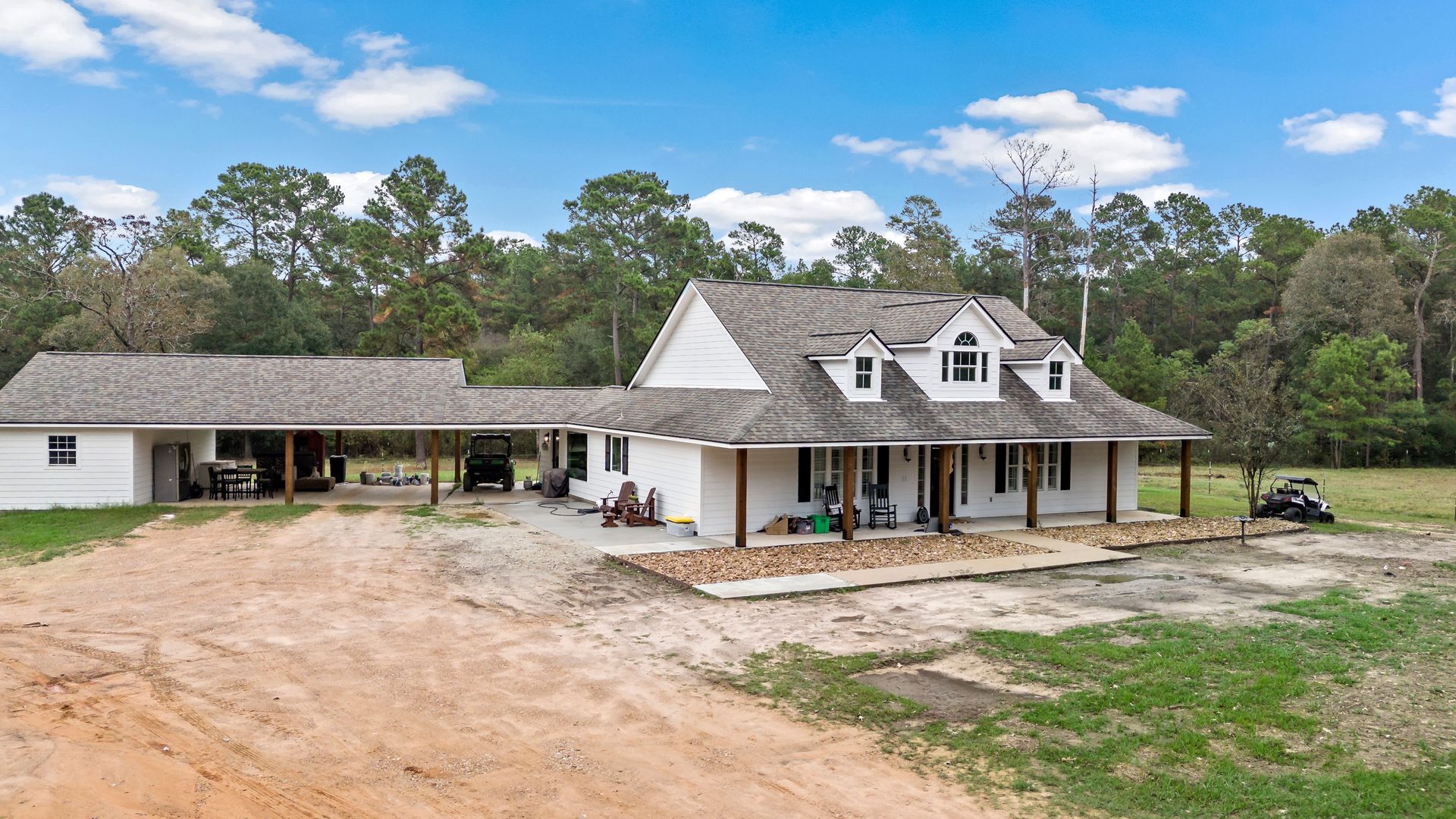 A large white house is sitting on top of a dirt road in the middle of a field.