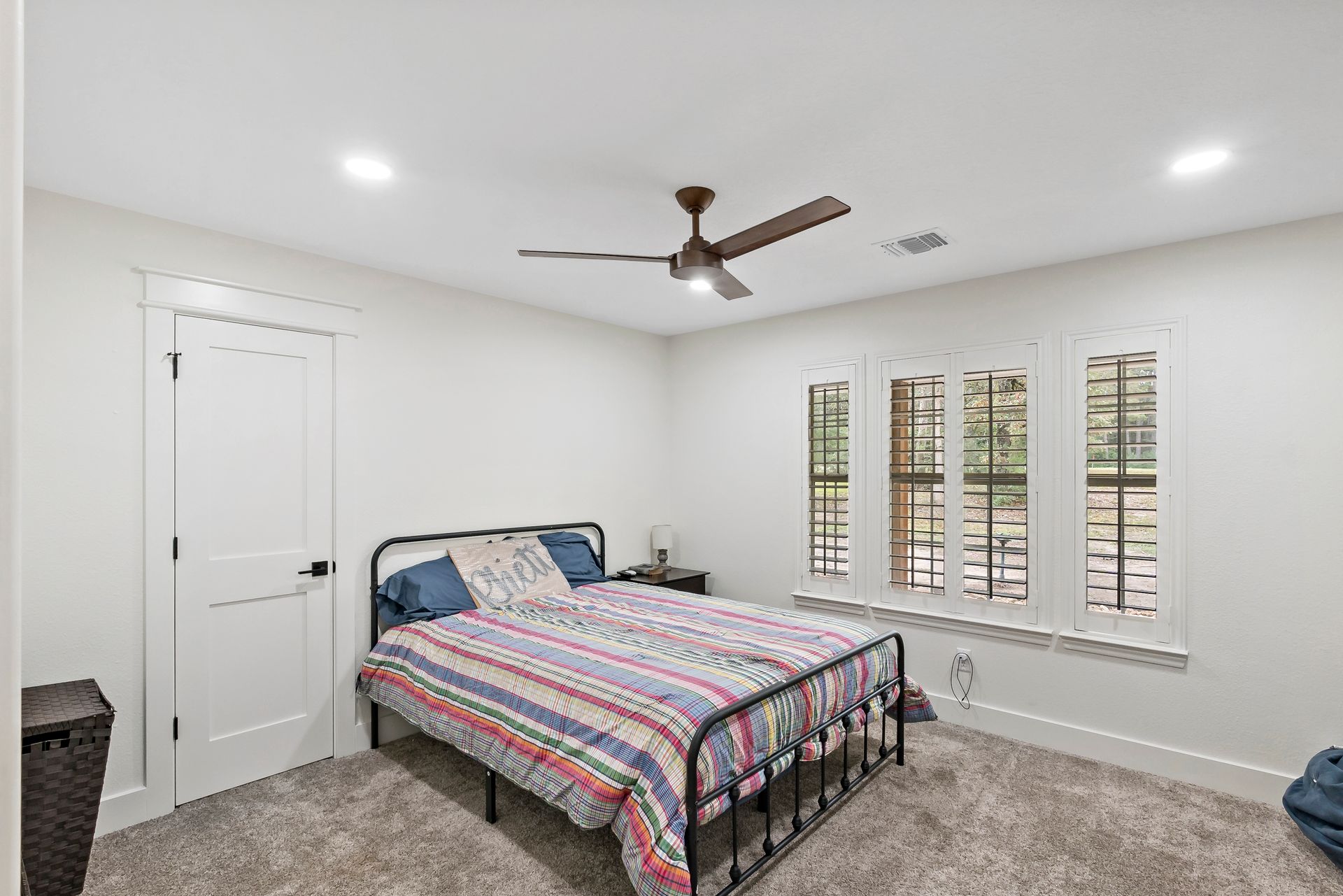 A bedroom with a bed , ceiling fan , and three windows.