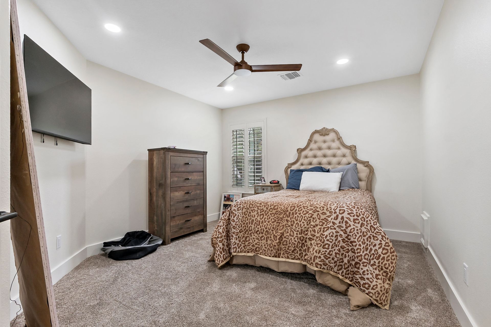A bedroom with a bed , dresser , television and ceiling fan.