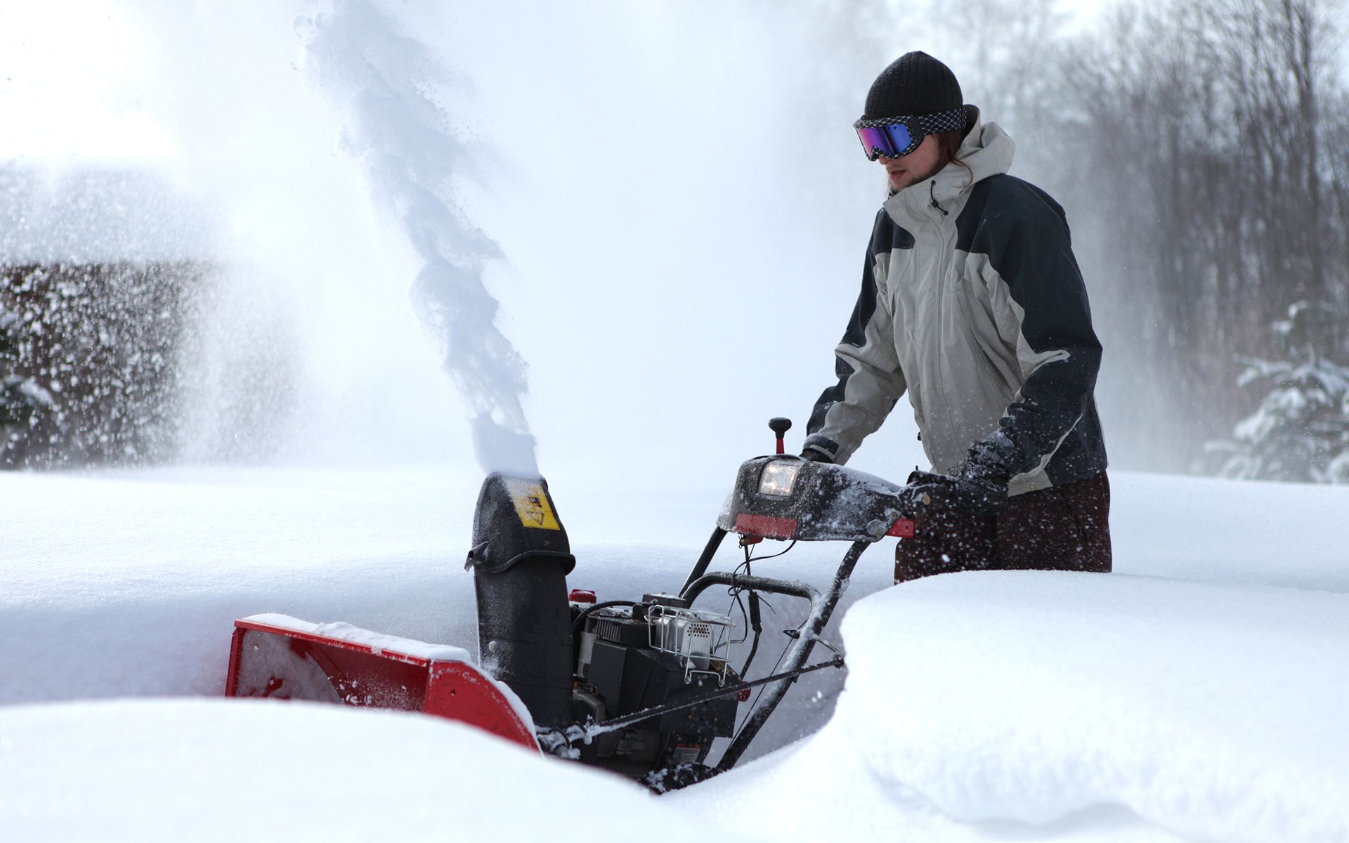 A man is using a snow blower to remove snow from a driveway.
