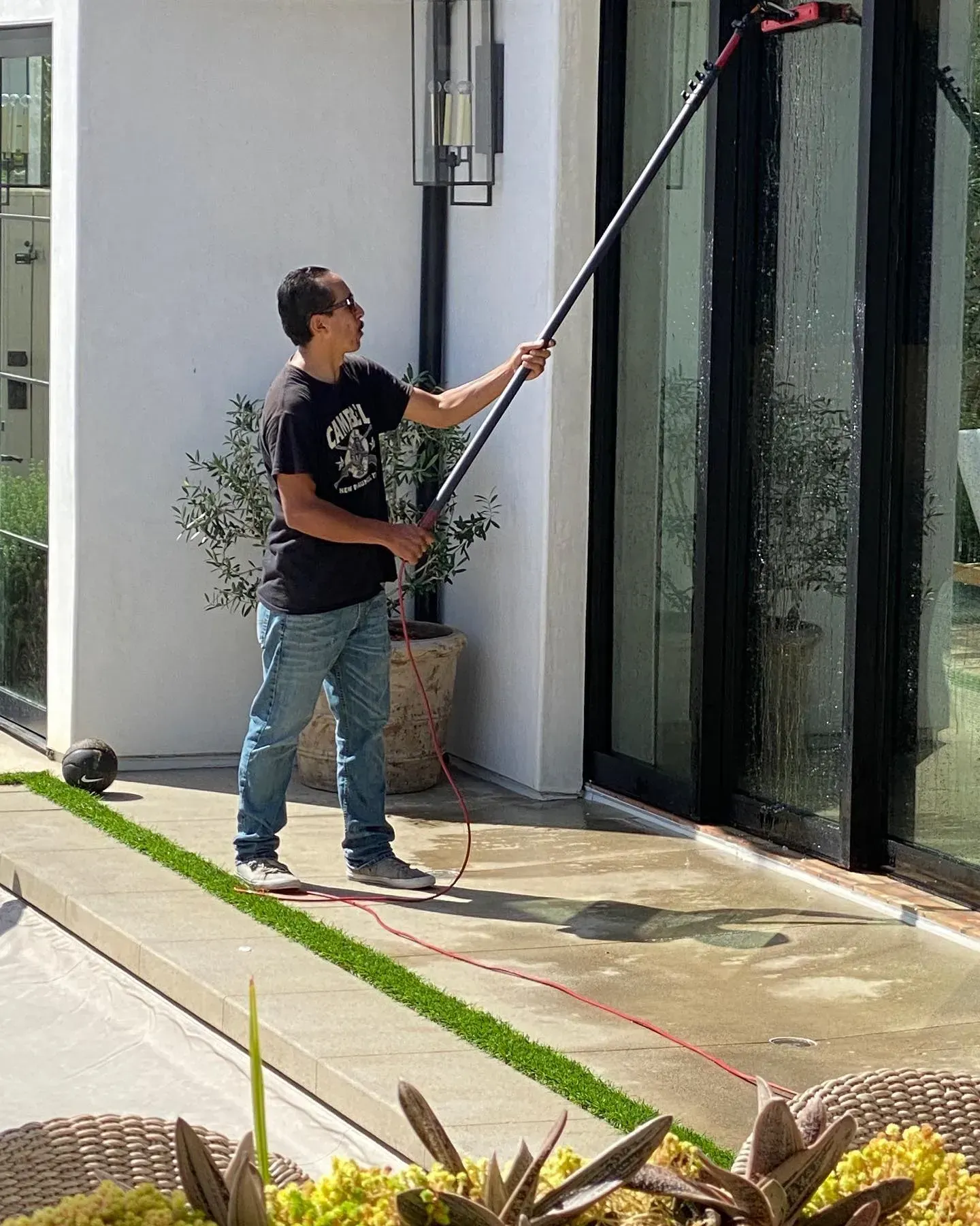 A man is cleaning a sliding glass door with a long pole.
