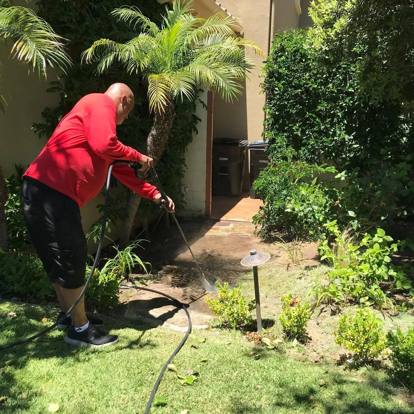 A man in a red shirt is using a pressure washer in a backyard.