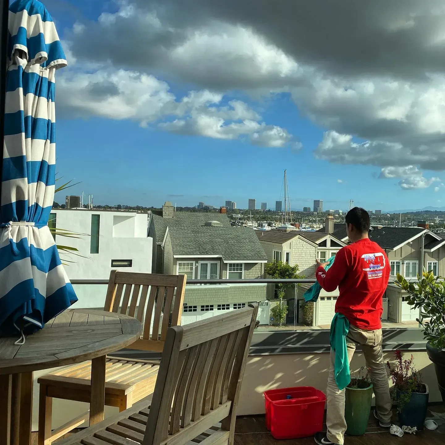 A man in a red shirt with the word cleaning on the back is cleaning a window
