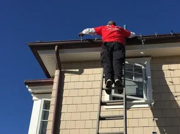 A man is standing on a ladder on the side of a house.