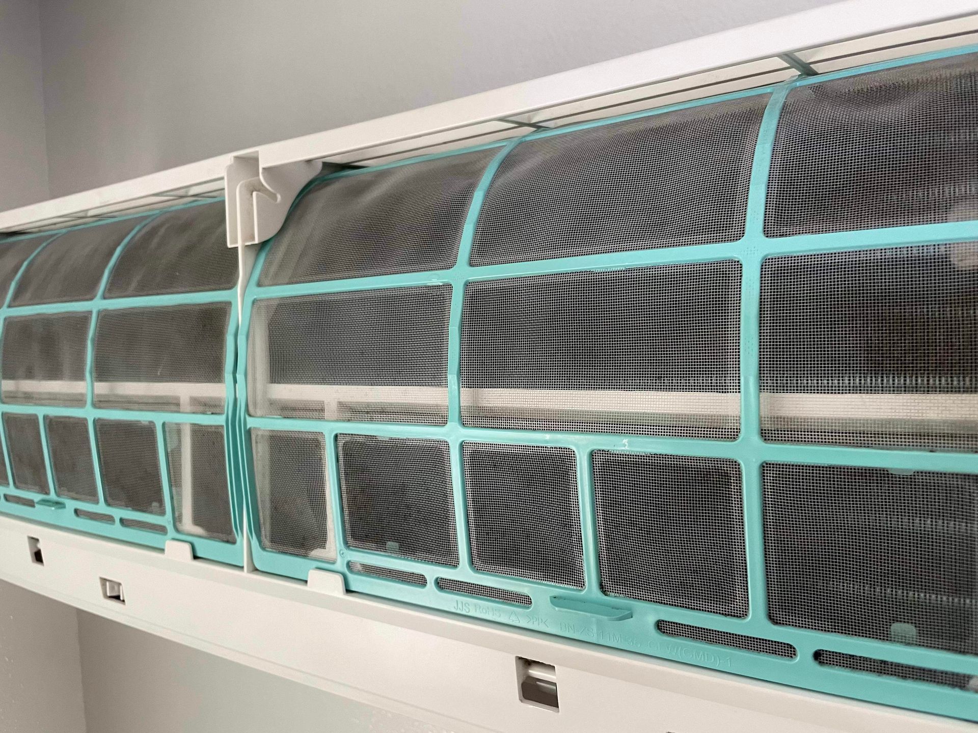 Air conditioner filter, dirty mesh grid within a white frame, indoors.