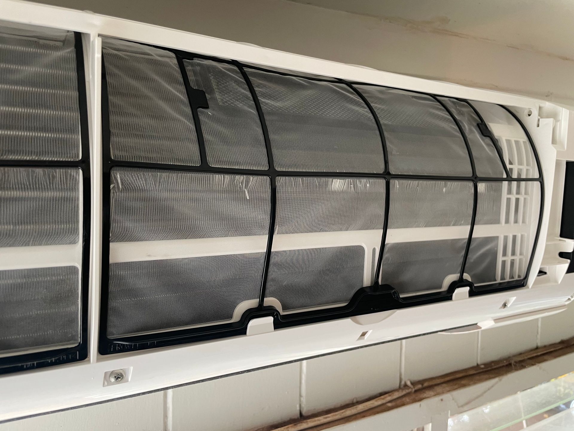 Air conditioner interior with exposed mesh filters, mounted on a white wall.