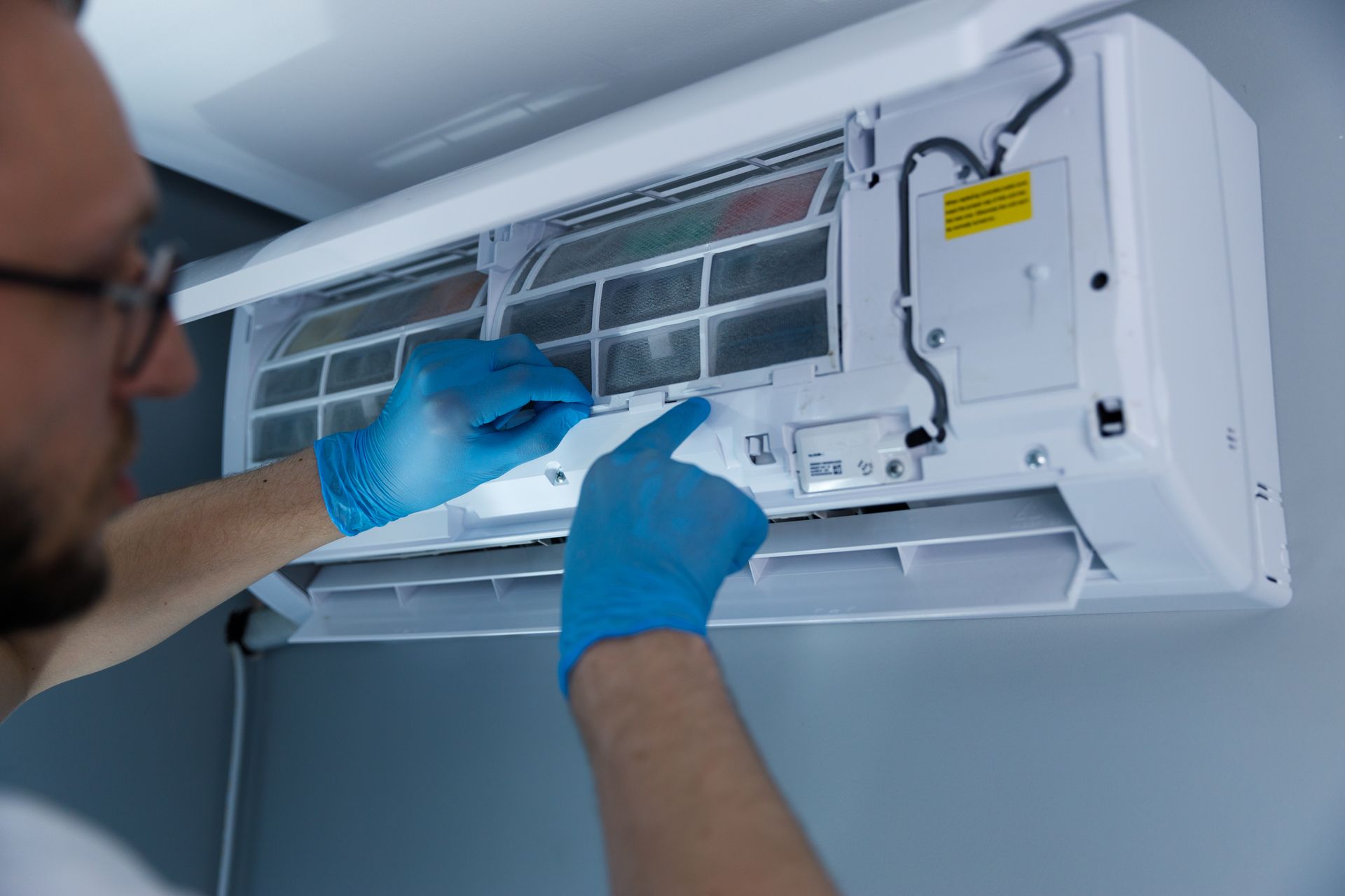 Person in blue gloves cleaning a wall-mounted air conditioning unit.
