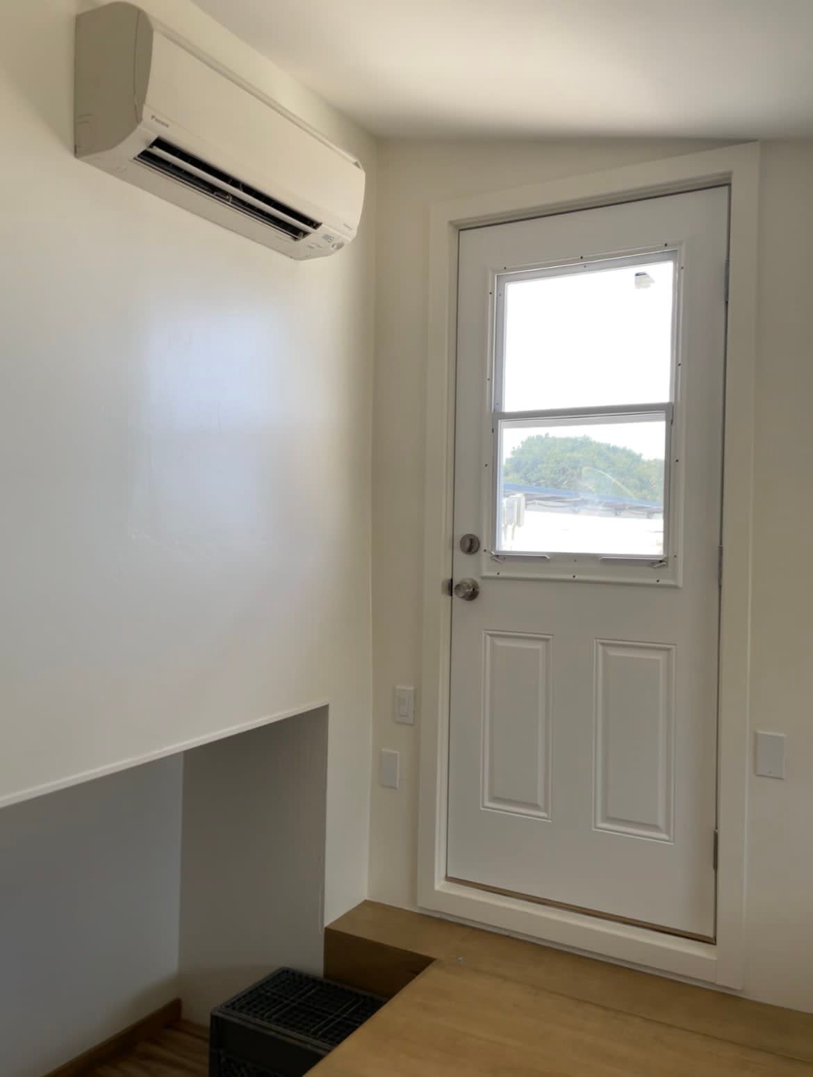 Interior room with air conditioner, white door, and light-colored walls.
