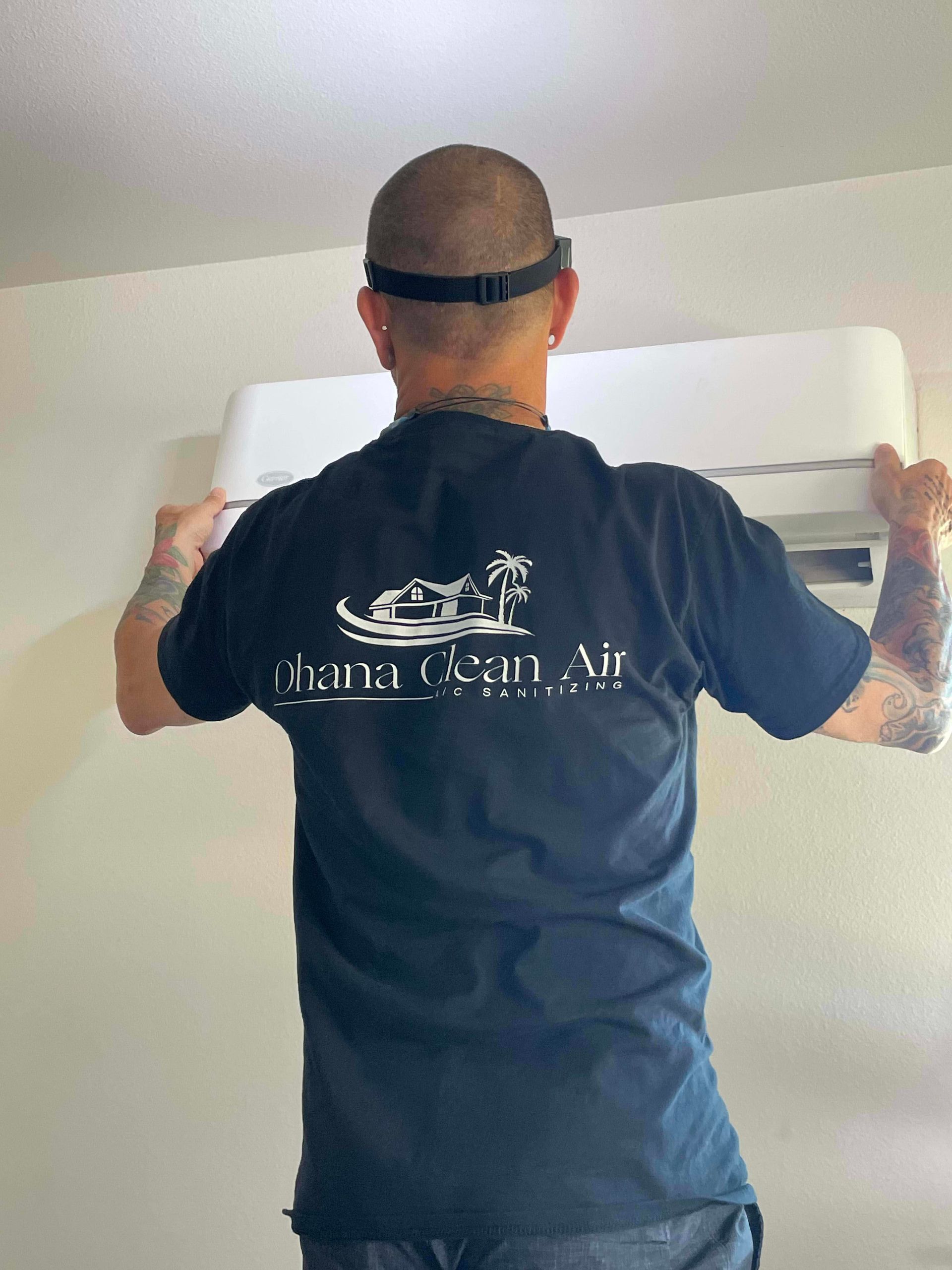 Man in a black shirt installing an air conditioning unit on a white wall.