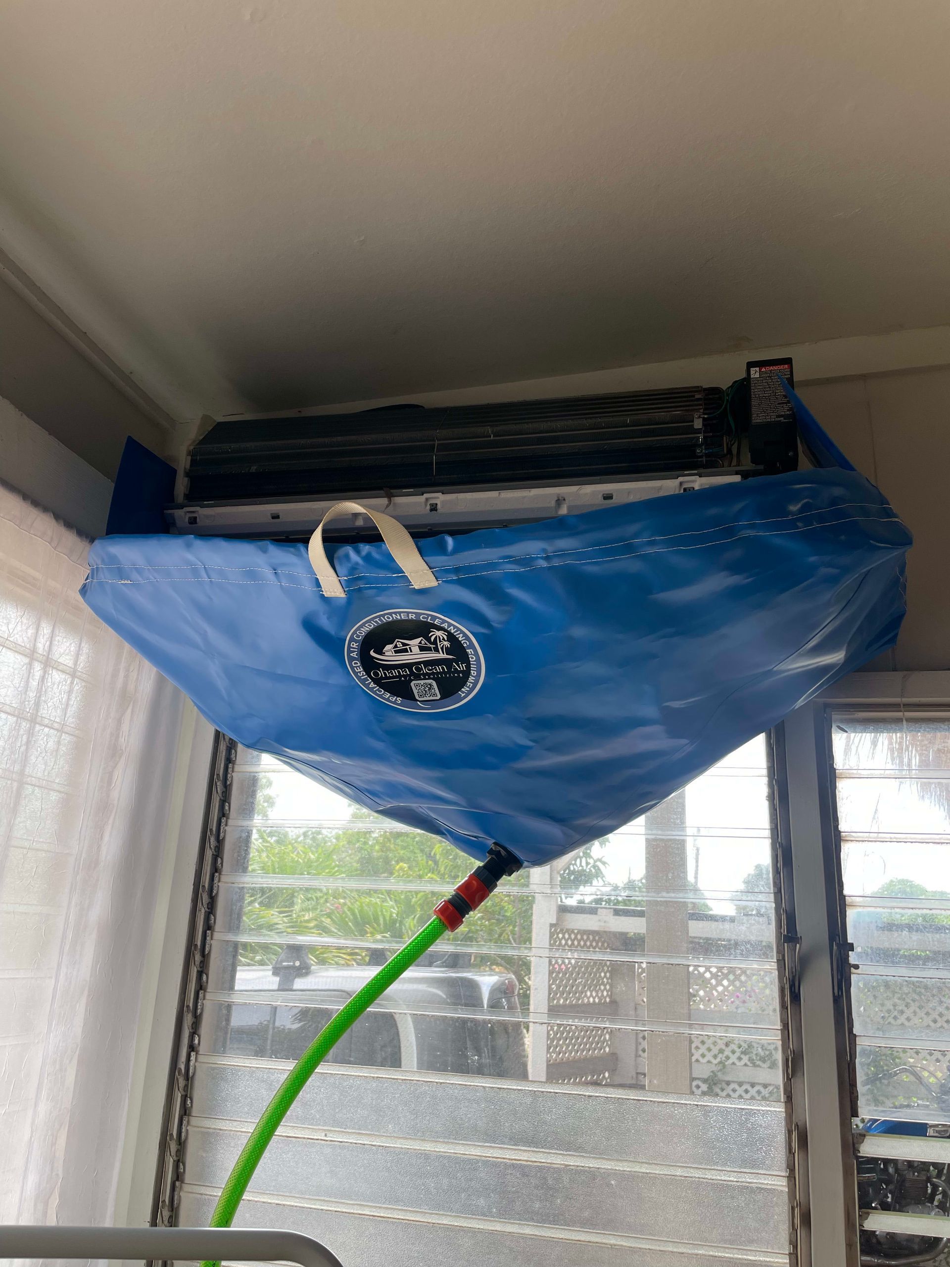 Blue water bag collects condensation from a window air conditioner; green hose drains the water.