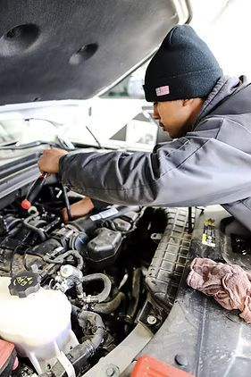 Mechanic working on a car engine with a wrench. Wearing a beanie, in a garage setting.