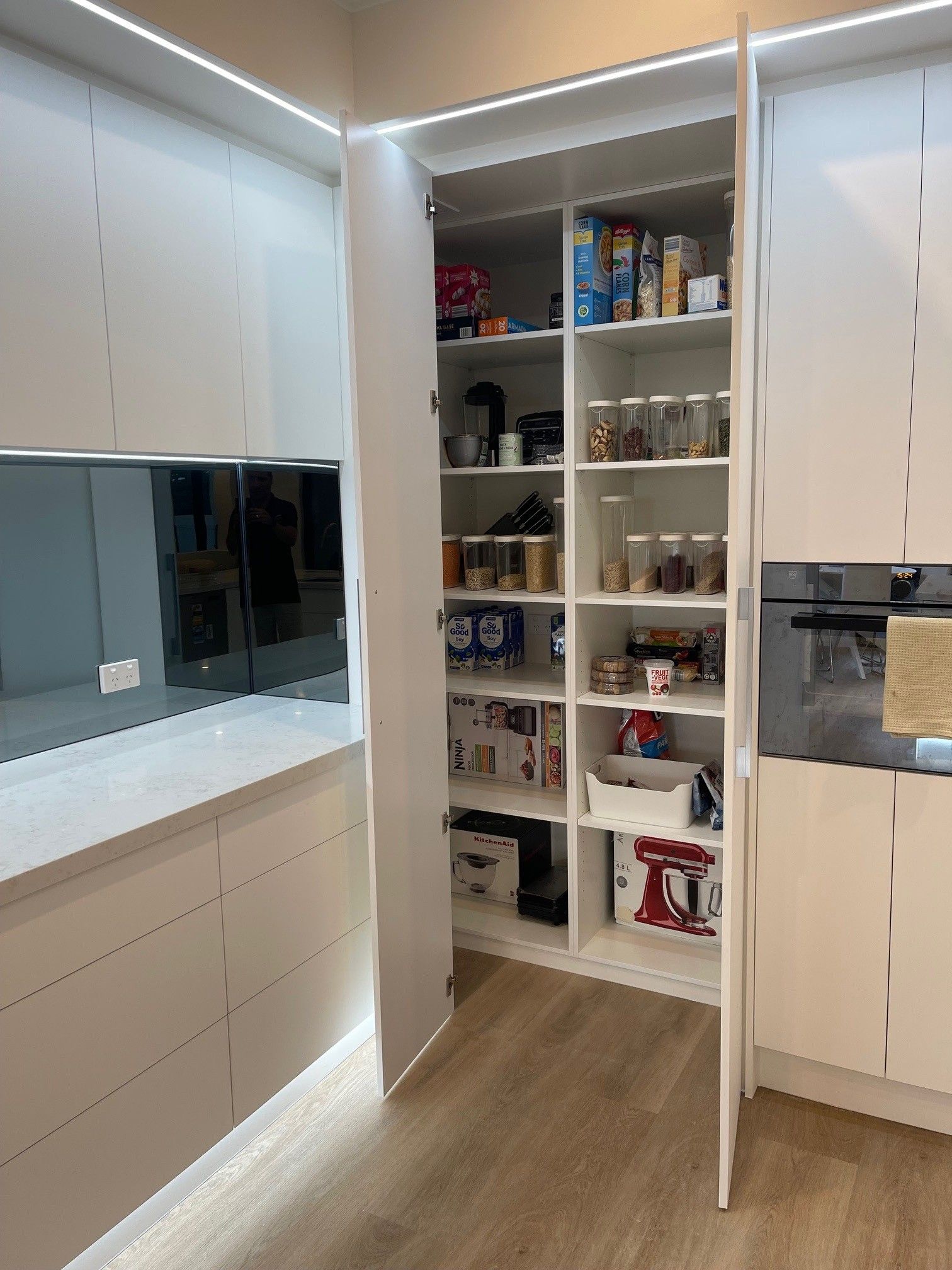 A kitchen with white cabinets and a pantry with the door open.
