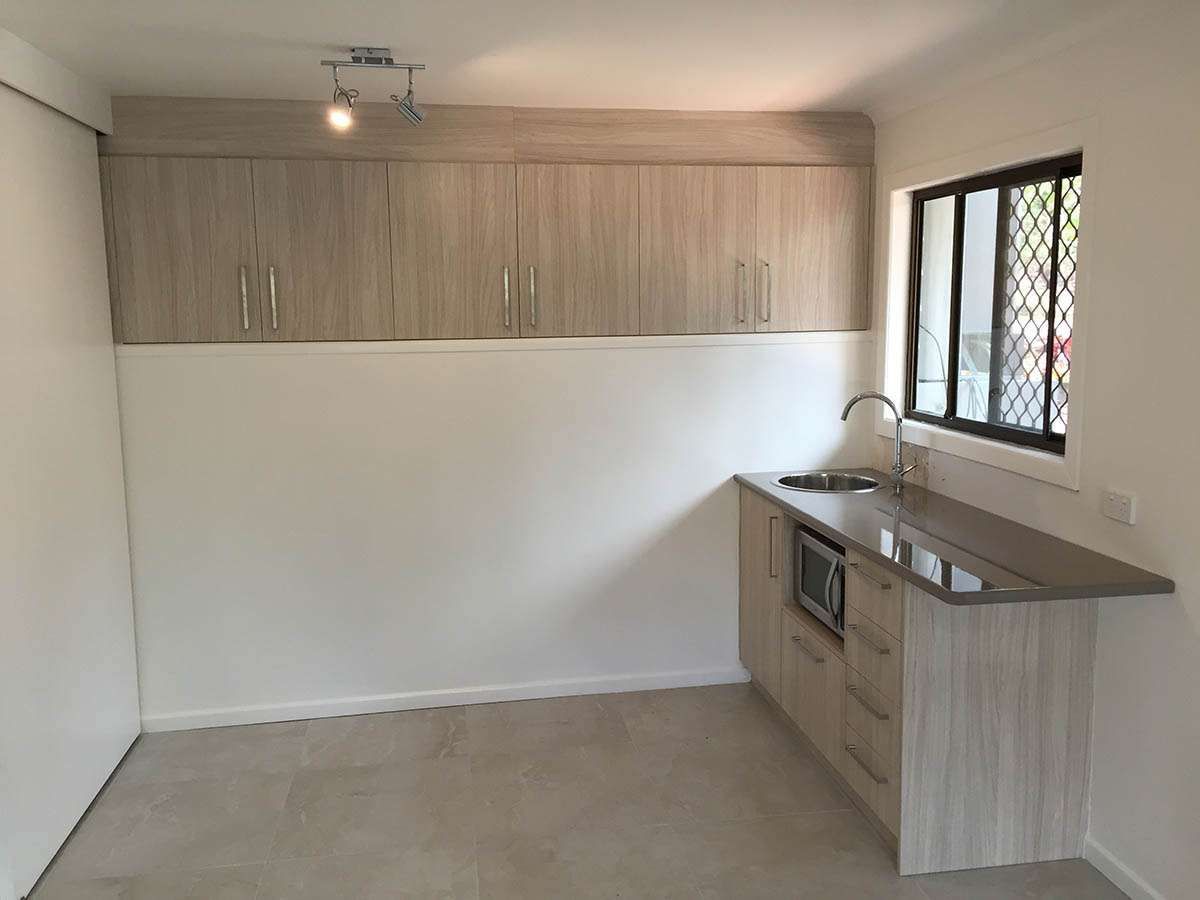 An empty kitchen with wooden cabinets and a window.