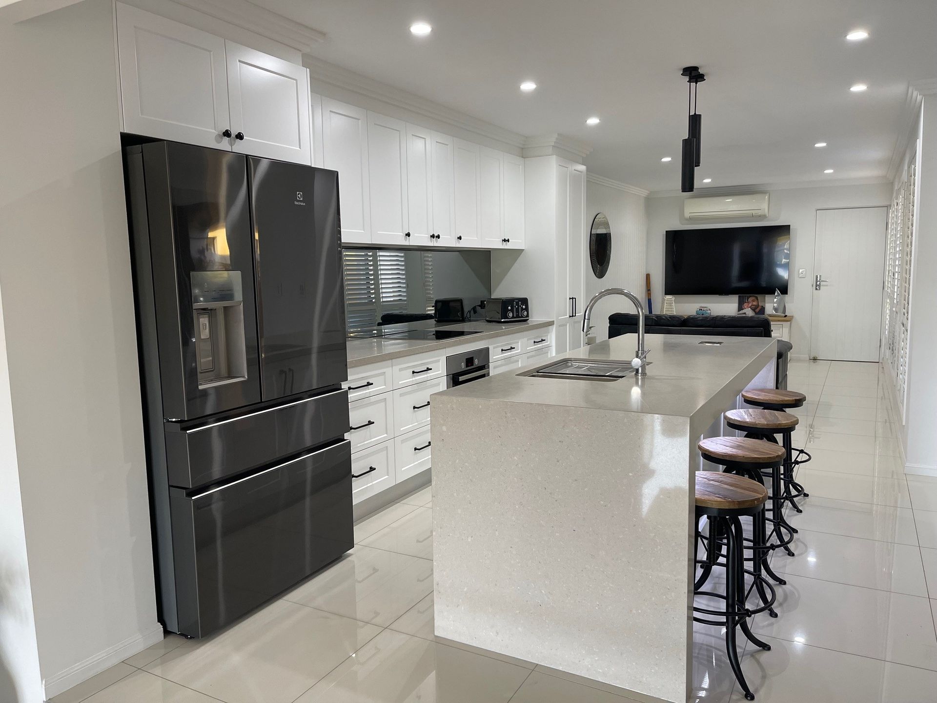 A kitchen with white cabinets , stools , a refrigerator and a television.