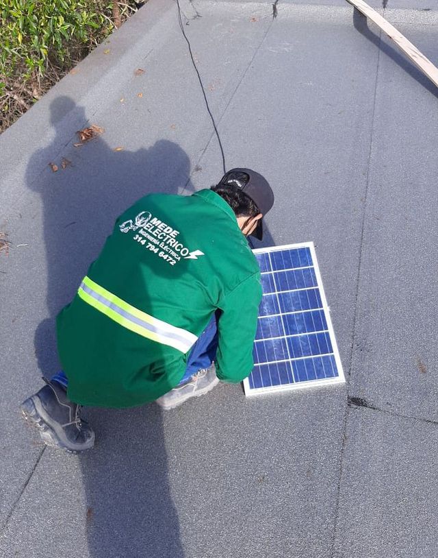 Un trabajador instala un pequeño panel solar en un tejado de tejas grises.