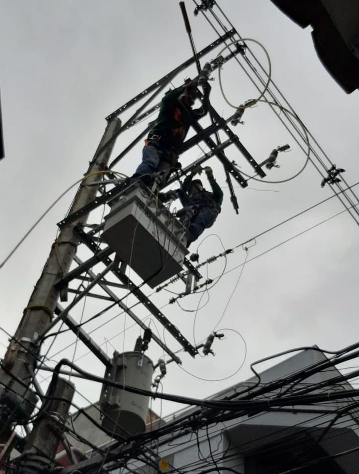 Trabajadores reparando líneas eléctricas en un poste de servicios públicos, rodeados de cables aéreos enredados.