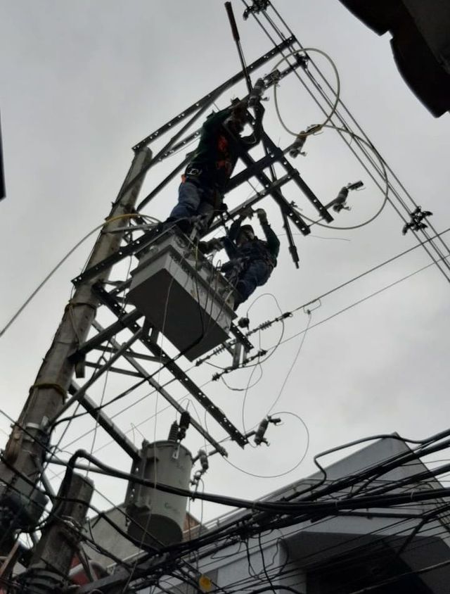Trabajadores reparando líneas eléctricas en un poste de servicios públicos, rodeados de cables aéreos enredados.