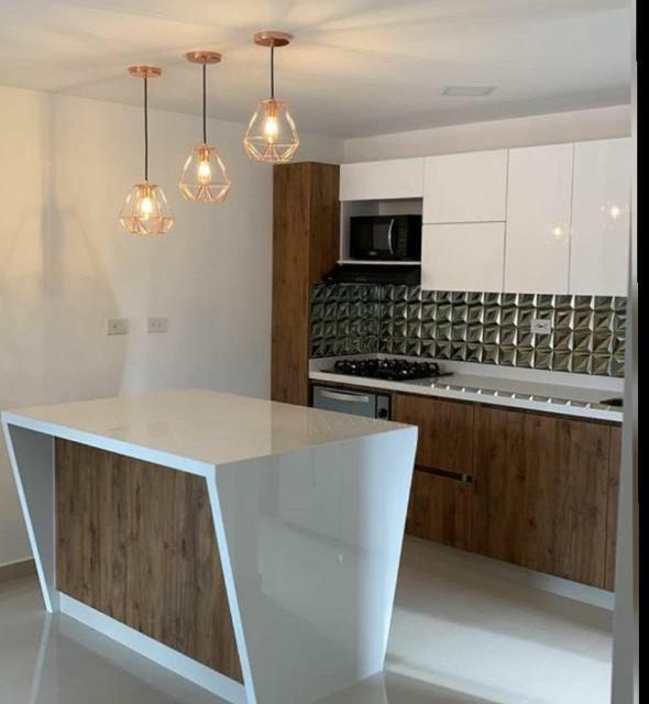 Cocina moderna con isla blanca, detalles en madera, lámparas colgantes de cristal y armarios brillantes.