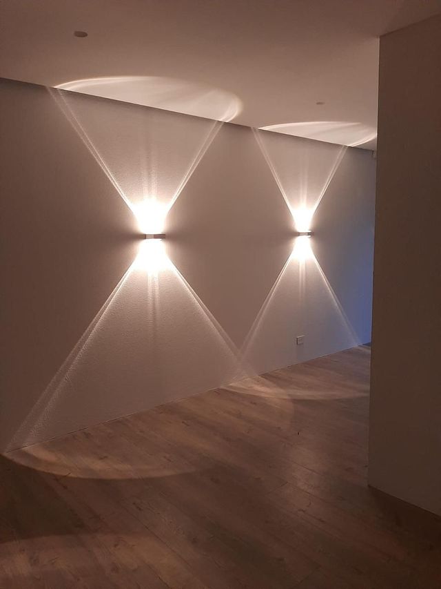 Pasillo moderno con suelo de madera y apliques de pared que proyectan patrones de luz en forma de abanico 