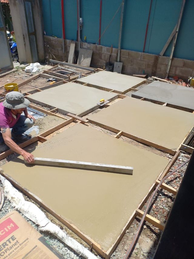 Obrero alisando losas de hormigón fresco en una obra con una llana larga.