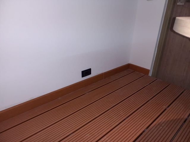 Rincón vacío con pared blanca, suelo de madera marrón y un enchufe de pared negro.