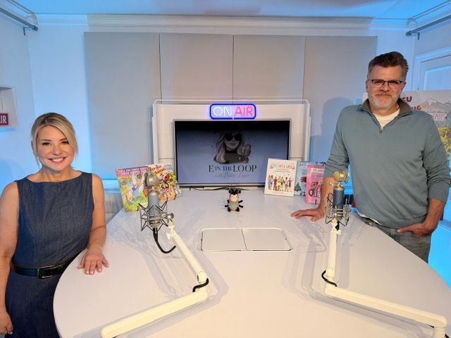 Two people at a podcast table; woman smiling, man with glasses, microphones, 