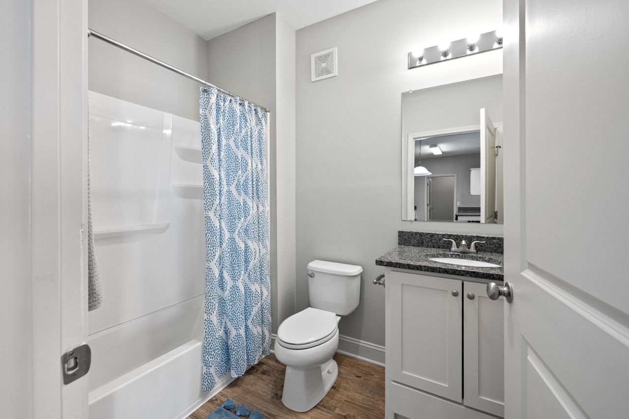Bathroom in a modern apartment with tub/shower, toilet, and a granite vanity.