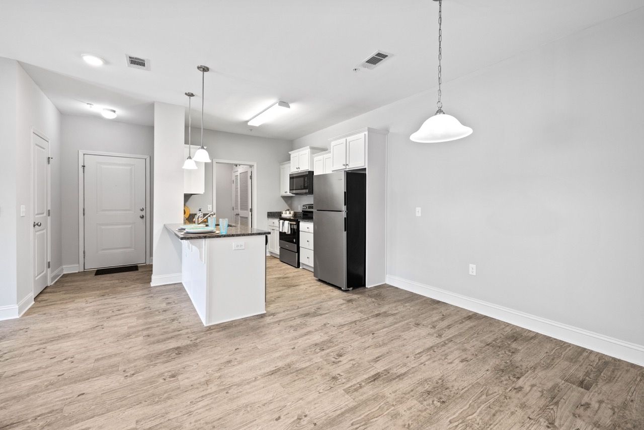 Open-concept kitchen and living area with an island, white cabinetry, stainless steel fridge, and wood-look flooring.