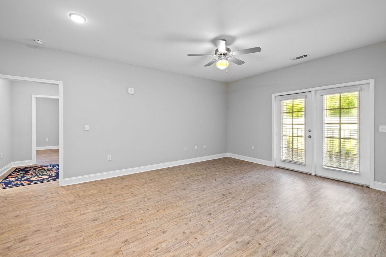 Empty apartment living room with laminate flooring, gray walls, a ceiling fan, and French doors to a balcony.