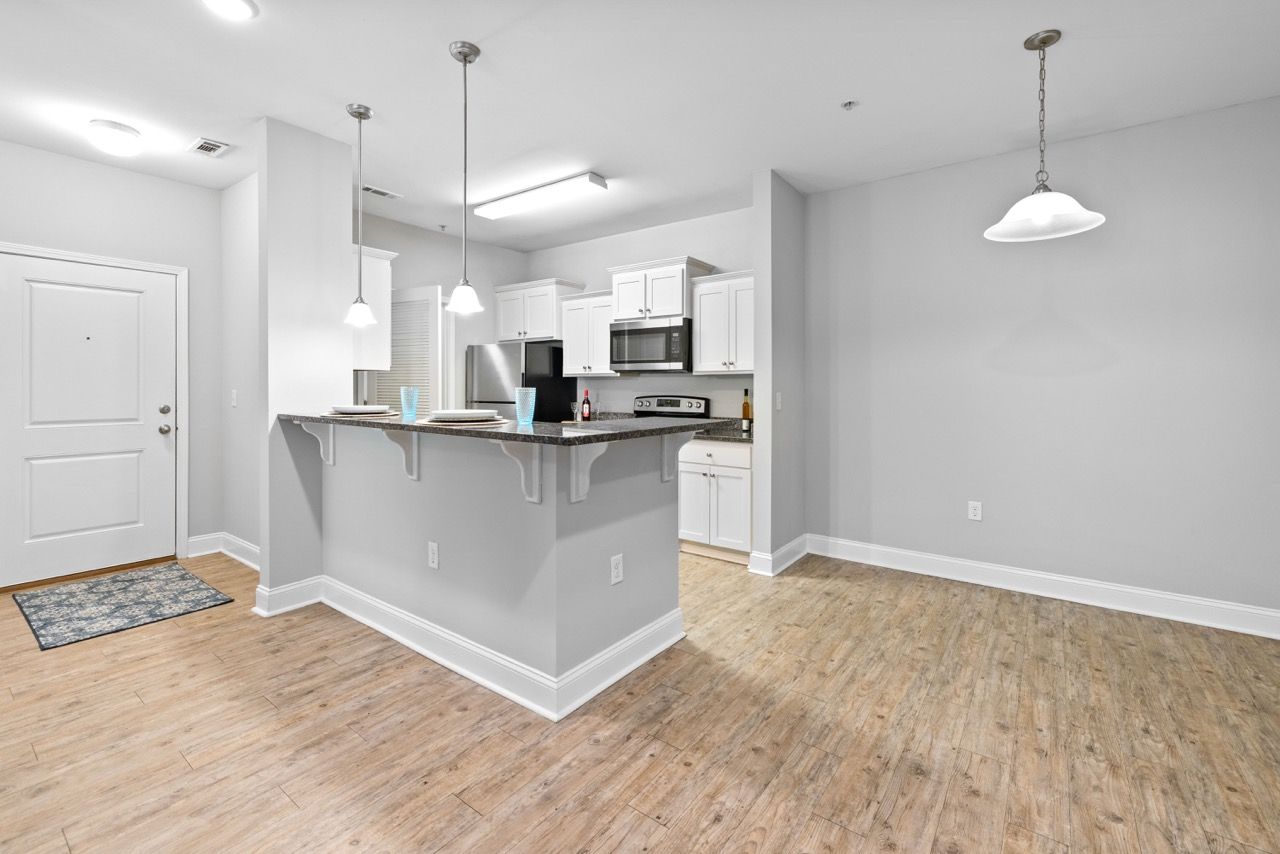 Open-concept kitchen with island, white cabinets, stainless steel appliances, and pendant lights.