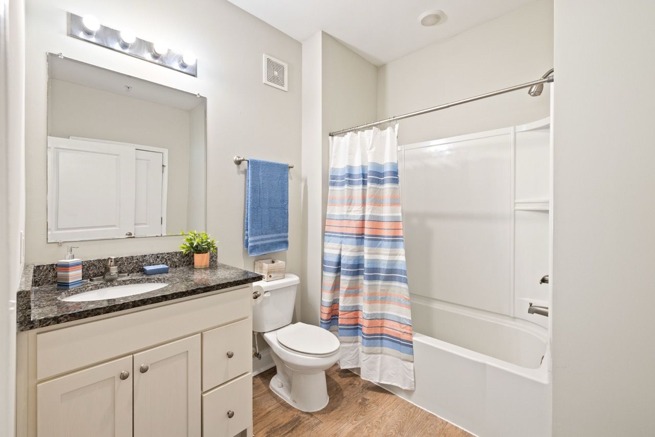 Bathroom in an apartment with a granite vanity, toilet, and striped shower curtain.