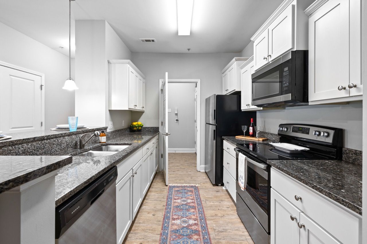 Galley-style kitchen in a modern apartment with white cabinets, granite countertops, and stainless-steel appliances.