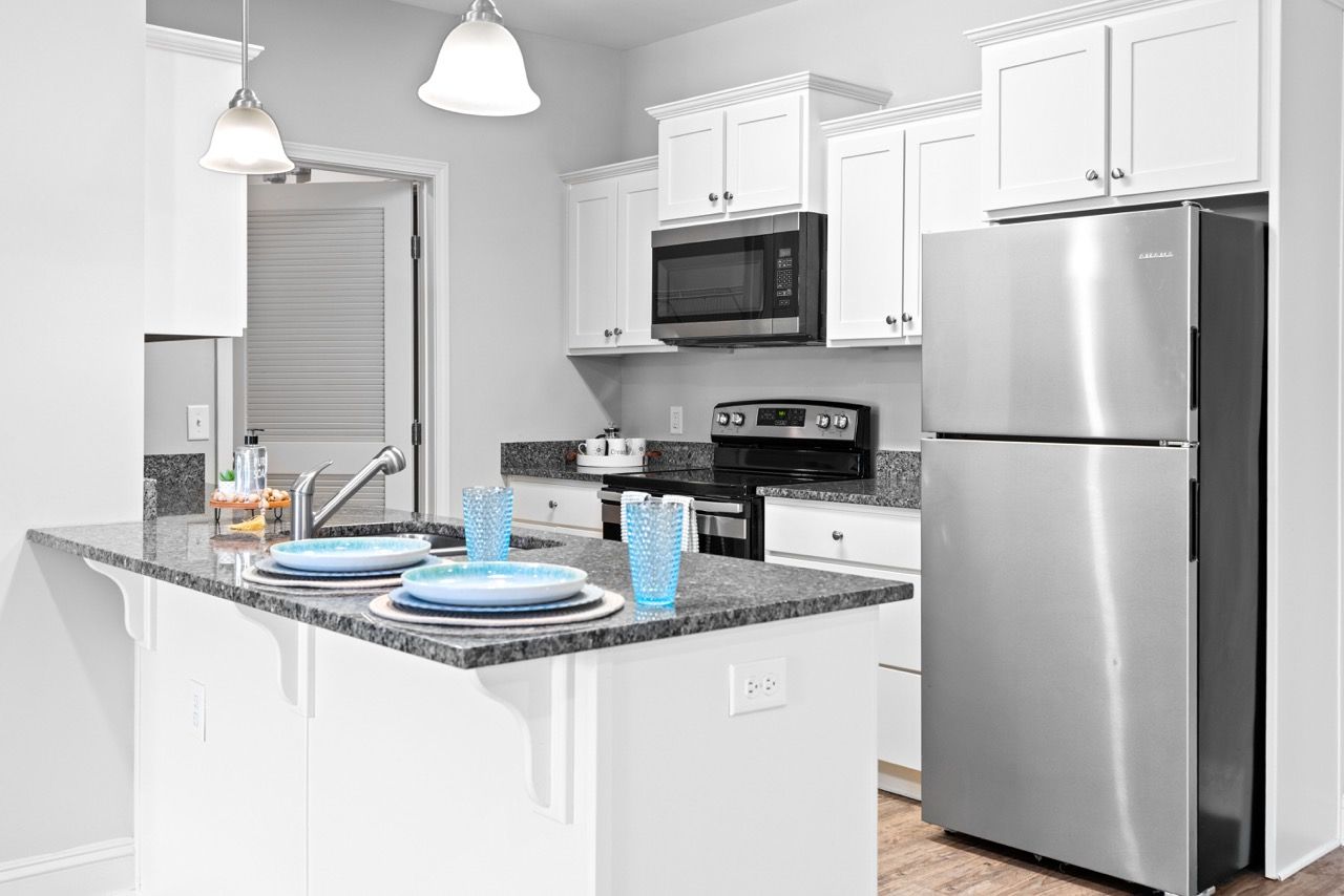 Modern apartment kitchen with white cabinets, granite countertops, and stainless steel appliances.