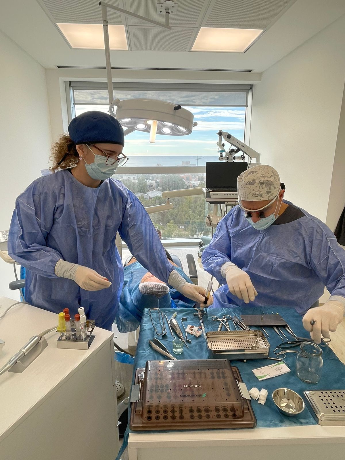 Dos profesionales dentales con uniformes y mascarillas trabajan con herramientas dentales cerca de un paciente