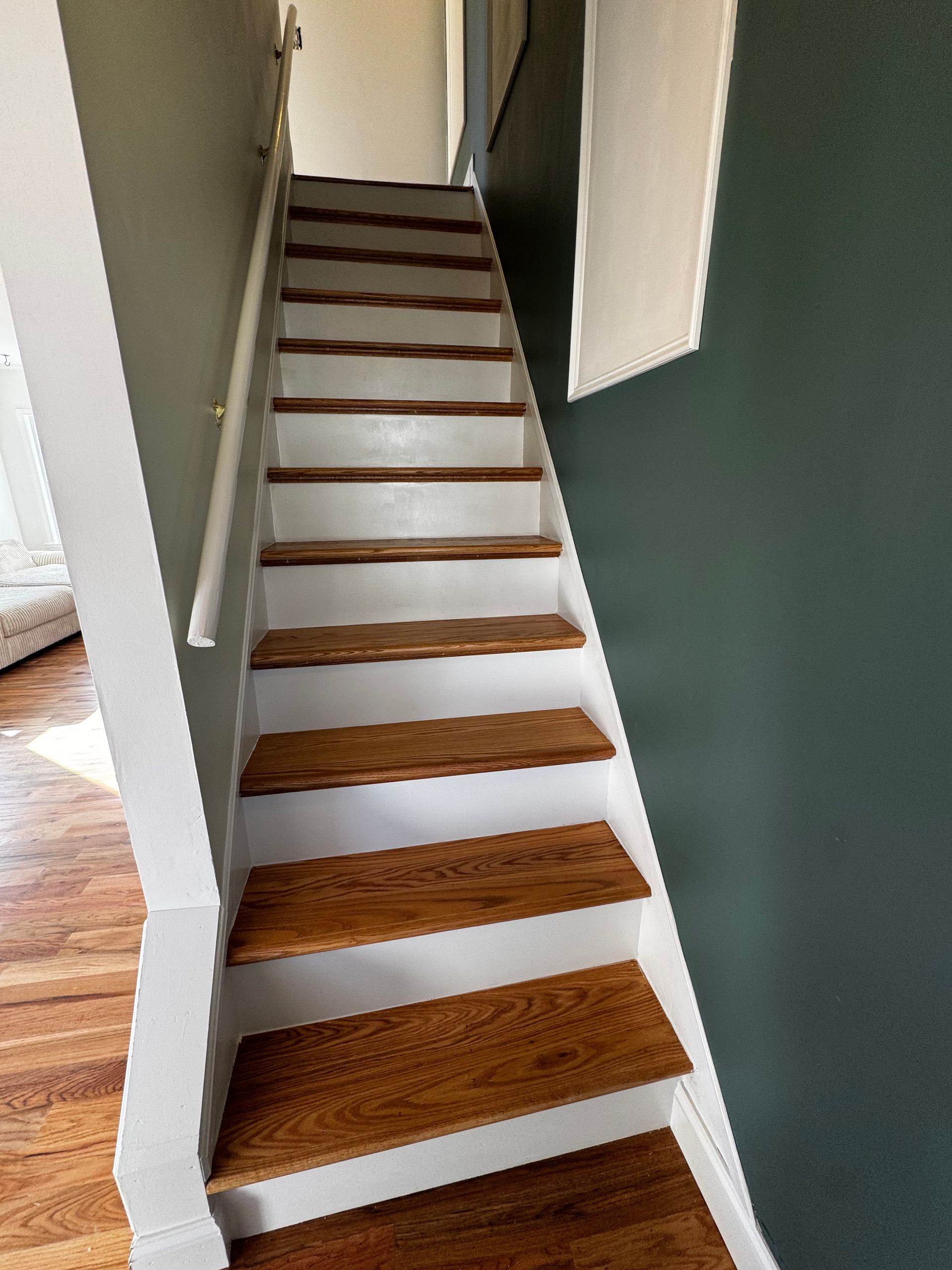 Wooden staircase with white risers and handrail, green and white walls.