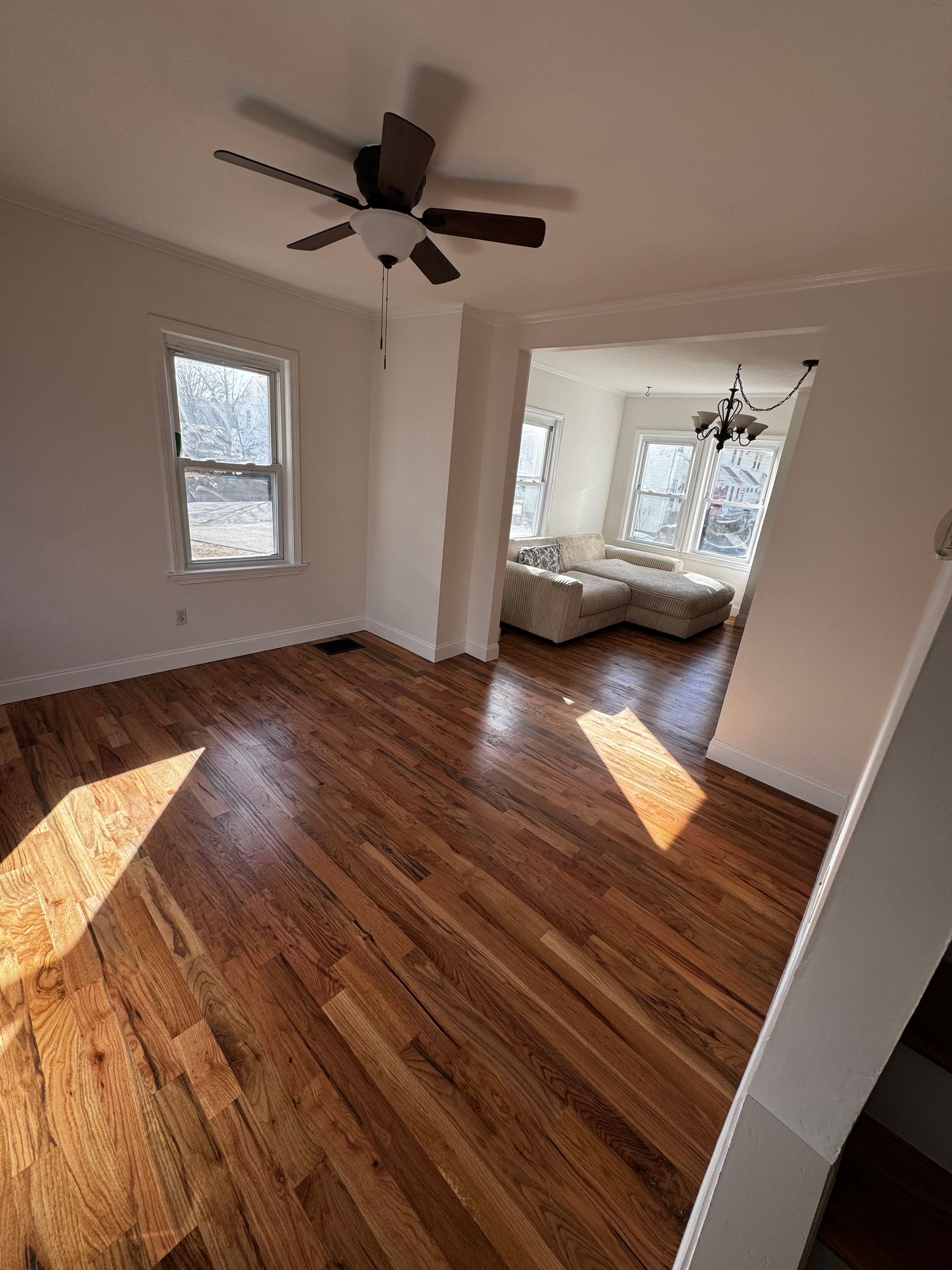 Living room with hardwood floors, white walls, and a view into another room.
