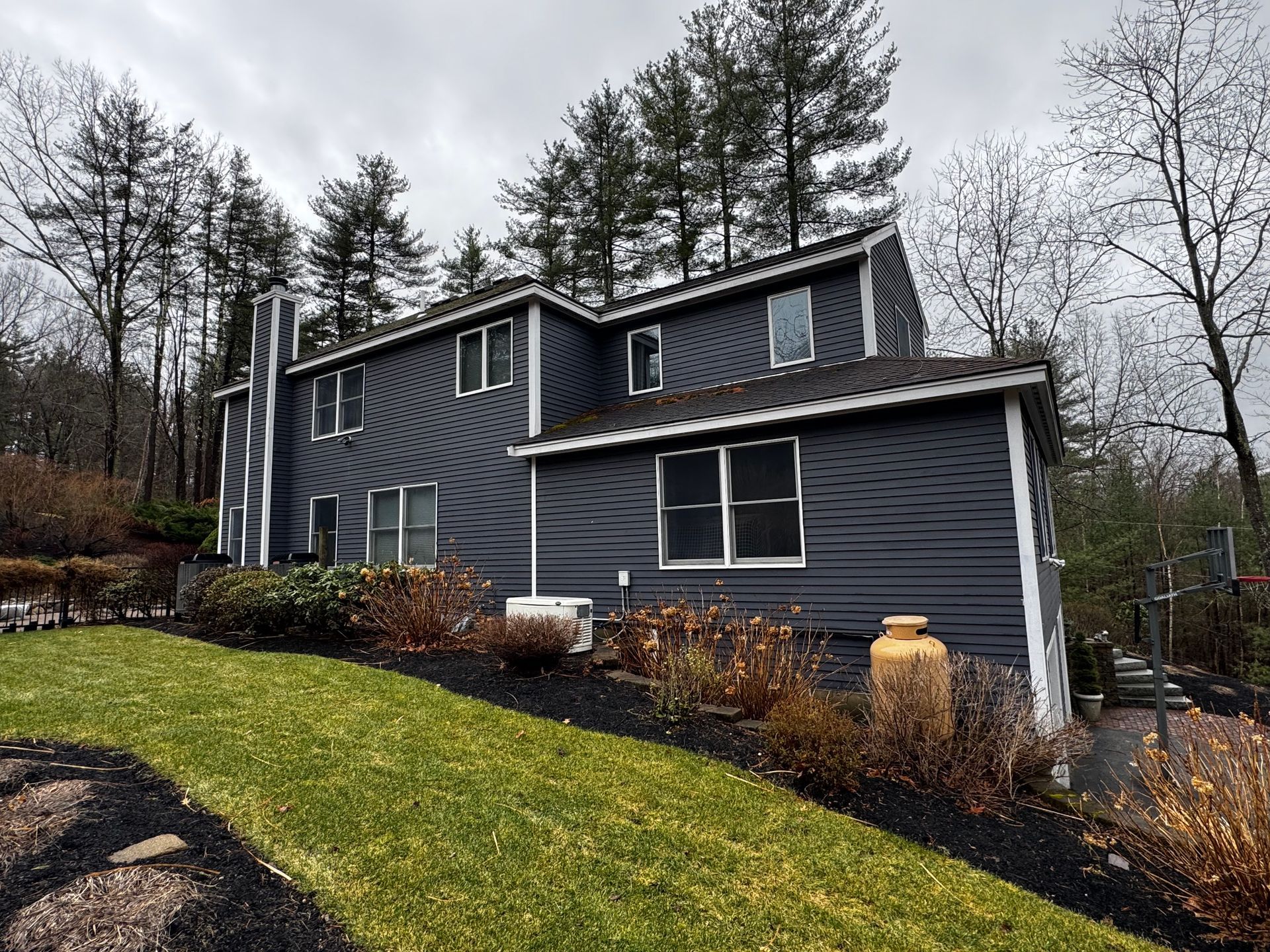 Dark gray house with white trim set on a green lawn with a tree-lined backdrop.