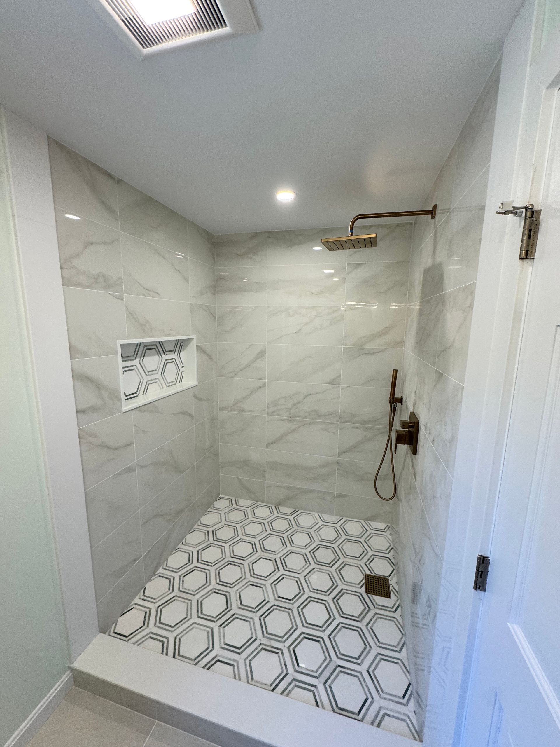 Modern shower with marble walls, hexagon tile floor, and bronze fixtures.