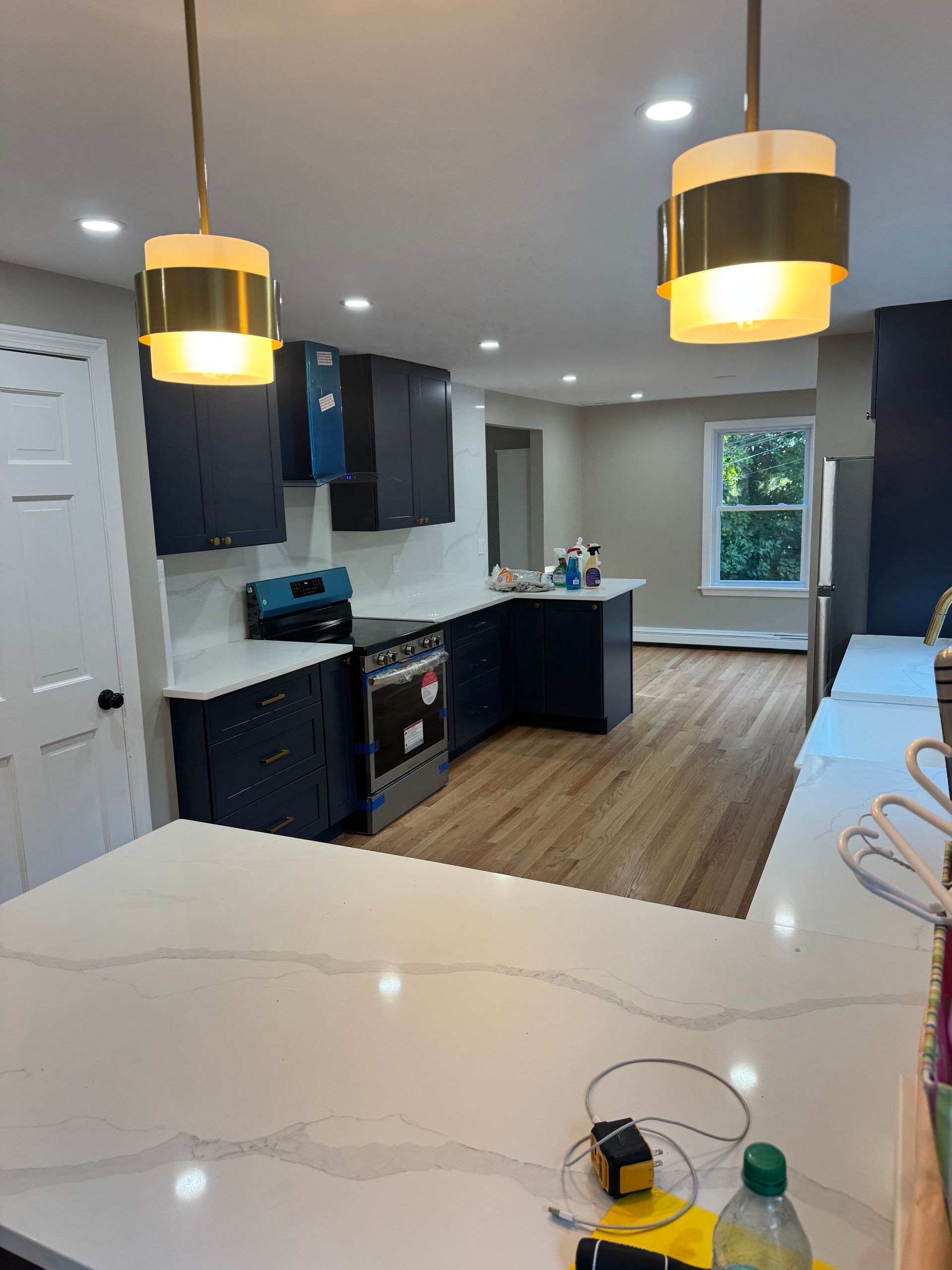 Newly renovated kitchen with dark blue cabinets, white countertops, and wood flooring. Two pendant lights hang above an island.