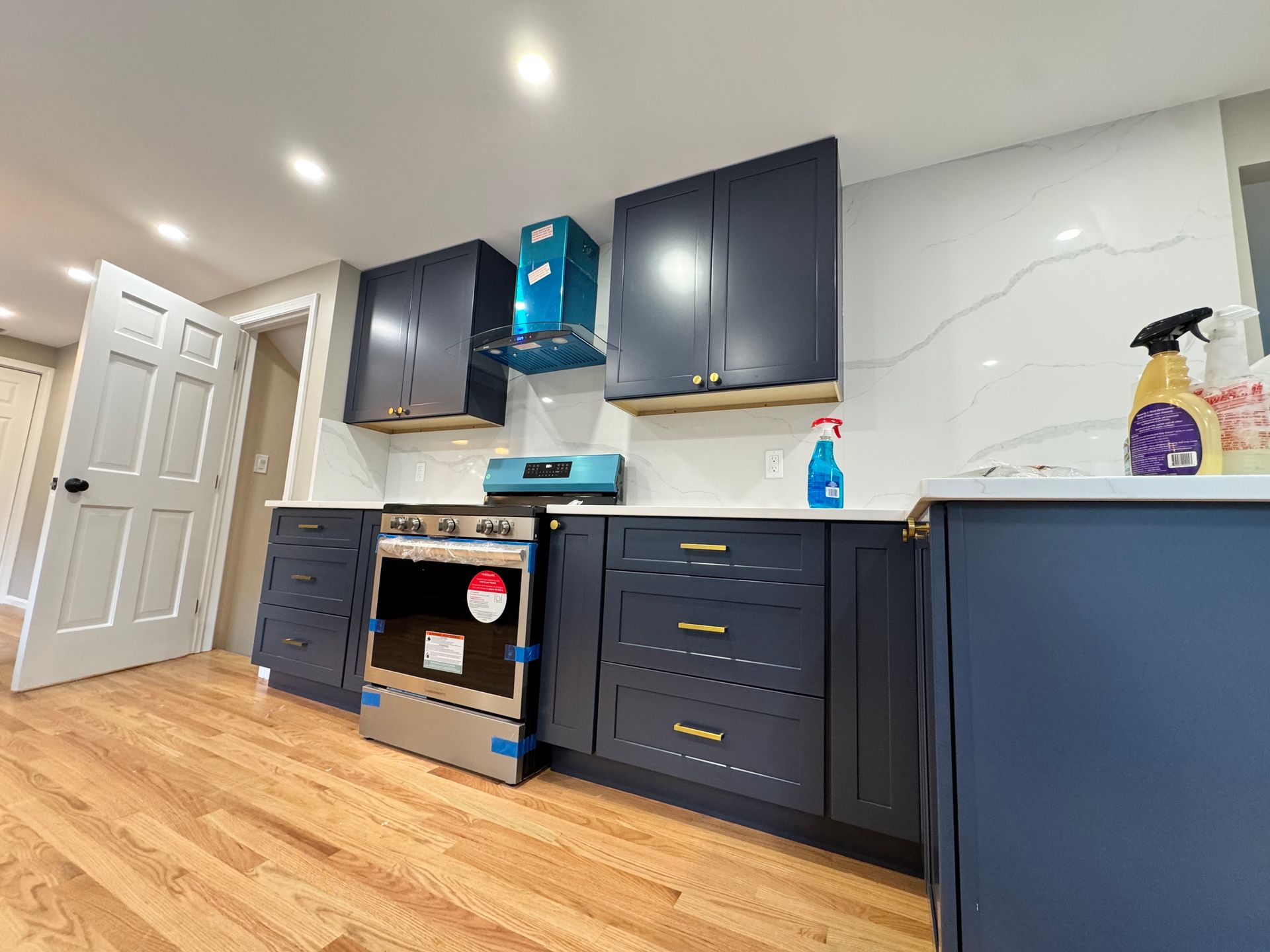 Newly renovated kitchen with dark blue cabinets, white countertops and backsplash, wood floor.