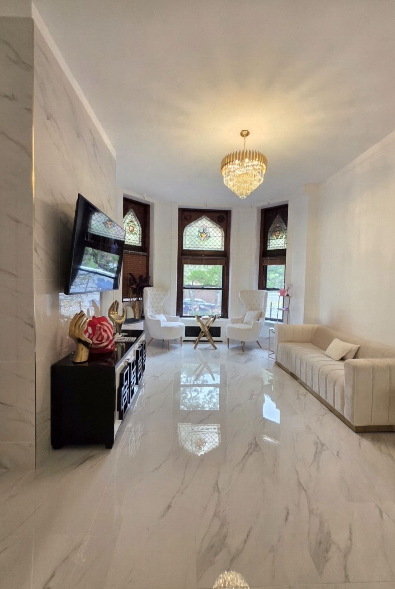 Living room with white marble floors, beige sofa, two armchairs, and a decorative chandelier.